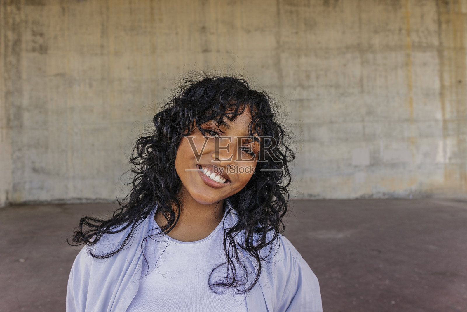 卷发年轻女子在水泥墙前微笑照片摄影图片