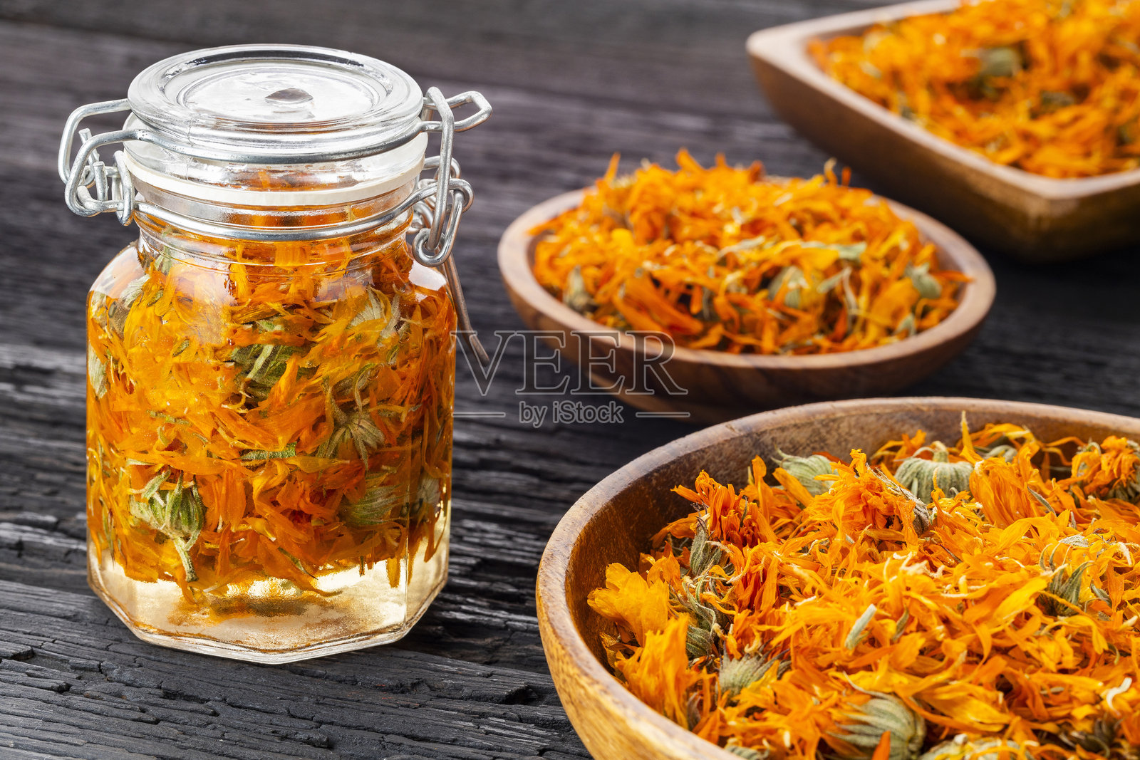 装有干燥金盏花和精油的玻璃罐，代表草药学和手工化妆品的自然概念。照片摄影图片