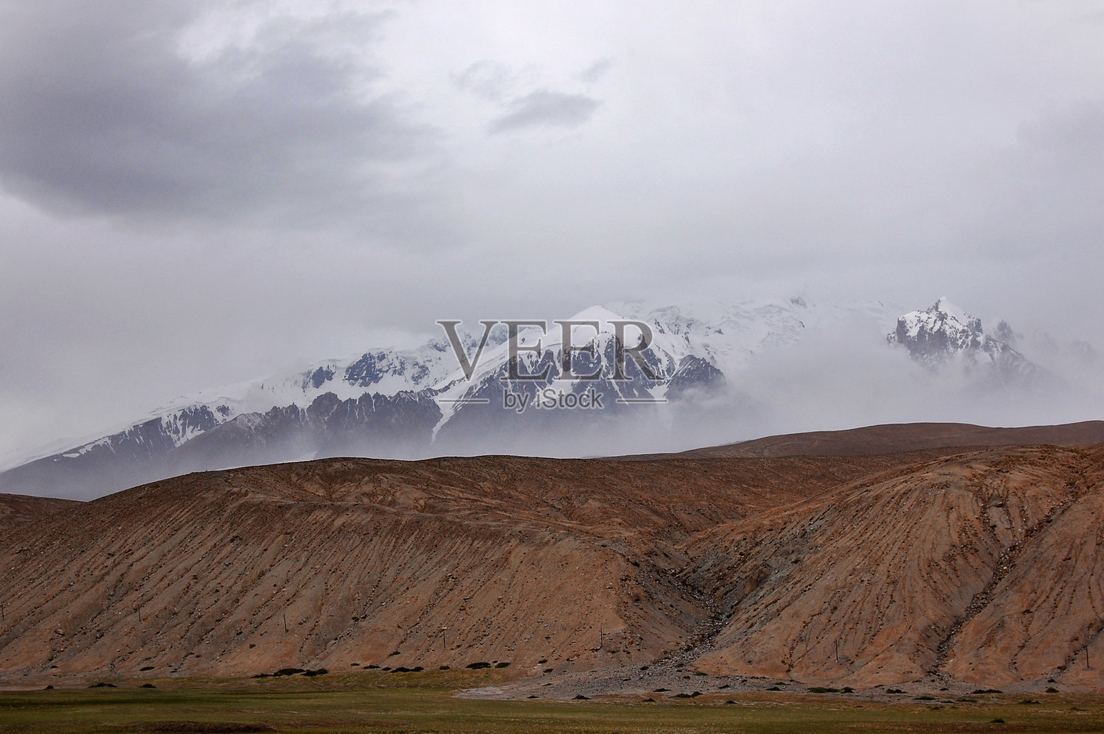 云层下的多云天空，雾气缭绕的雪山和干旱的景观照片摄影图片