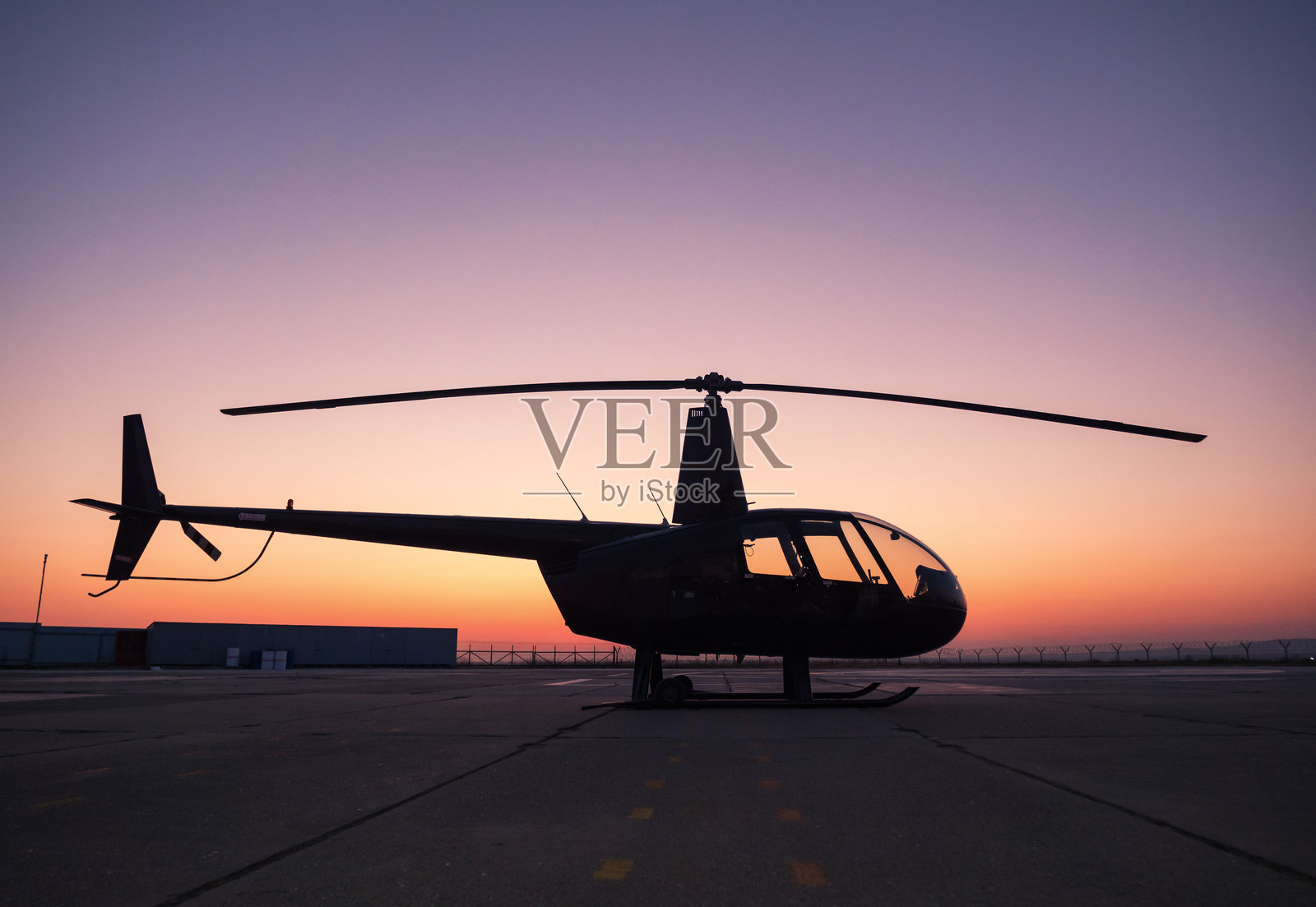 日落时分，一架黑色直升机停在地面上。照片摄影图片