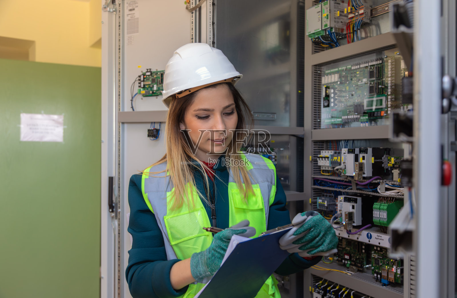 女工程师在发电站检查控制面板并做安全与维护记录照片摄影图片