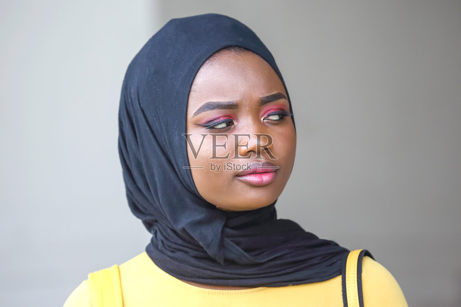 一名非洲女子头戴黑色头巾，妆容鲜艳，在白天位于公共场所照片摄影图片