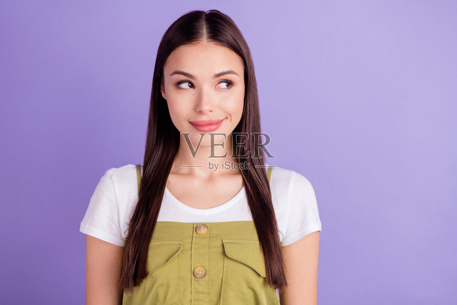 身穿白色T恤的年轻女子，表情狡黠可爱，对着虚空微笑，背景是孤立的紫色。照片摄影图片