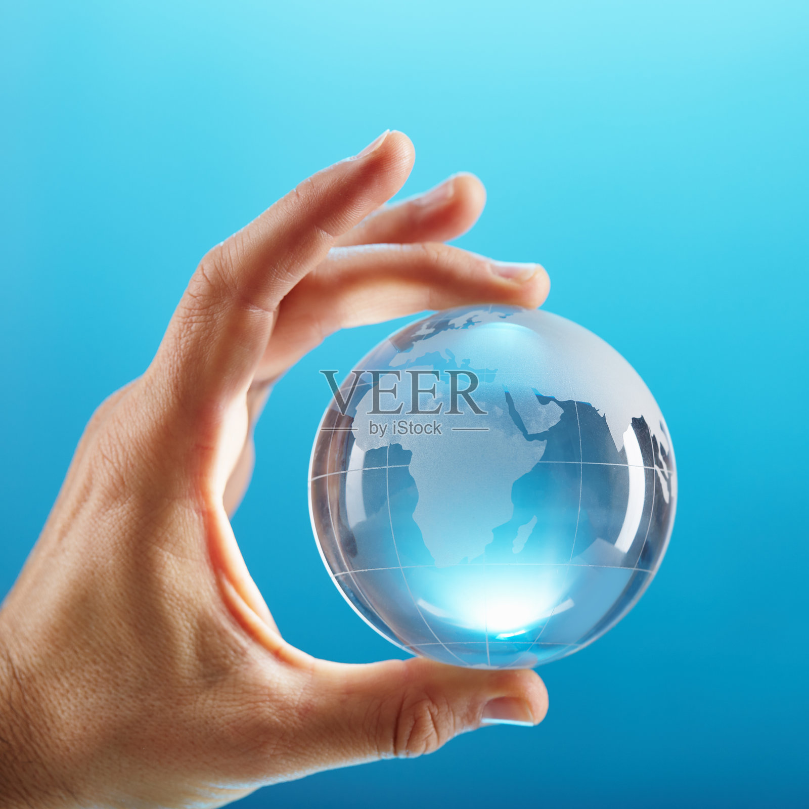 蓝色的背景前，一只手拿着一个明亮的玻璃地球仪照片摄影图片