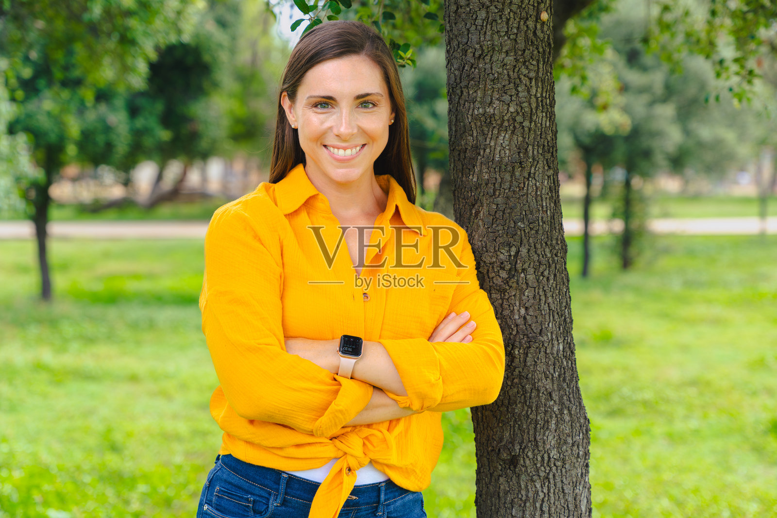微笑的女性在公园里双臂交叉站立，看向镜头照片摄影图片