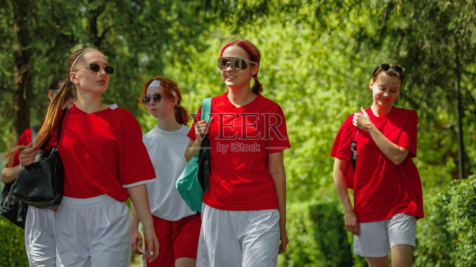 身穿红色球衣、戴着太阳镜的女子足球队自信地走在公园里照片摄影图片
