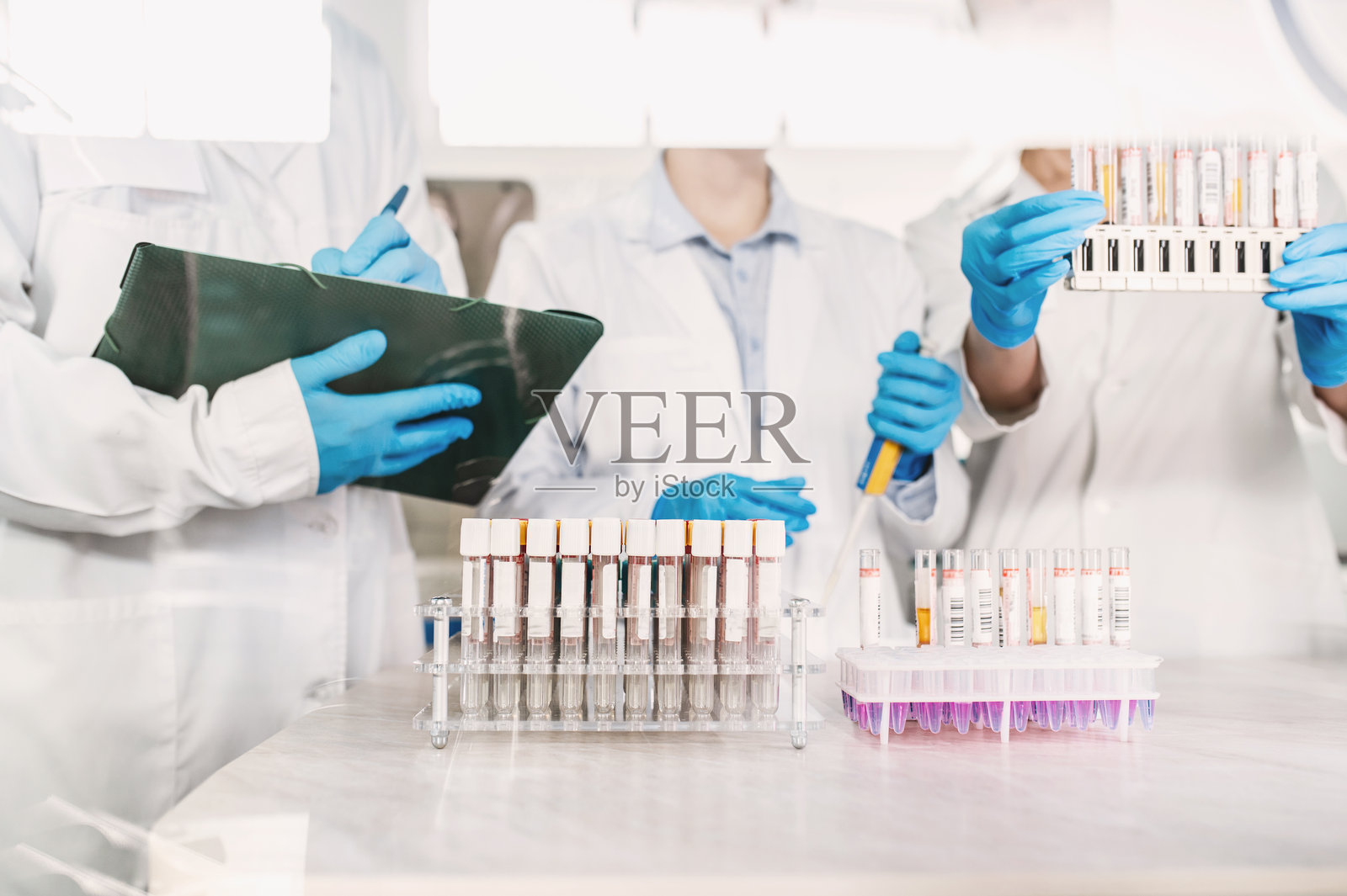 一群身穿白大褂、戴着一次性手套的匿名人士在现代生物实验室里进行研究。医生们在实验室里进行检测。照片摄影图片