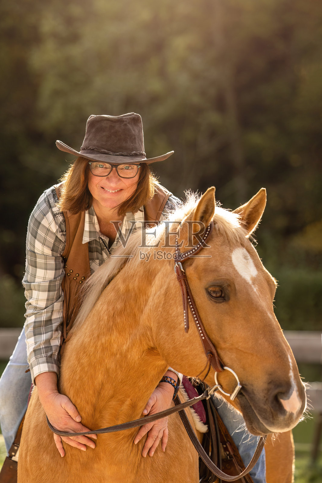 身着西部装备的年长女性，在温暖的阳光下放松地坐在她的枣骝色夸特马阉马旁，面带微笑。照片摄影图片