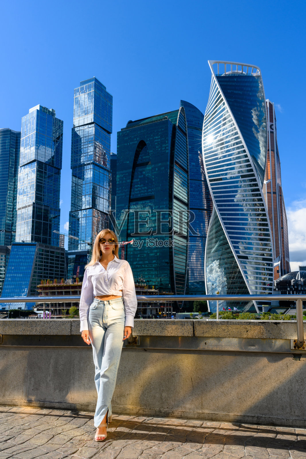 阳光明媚的城市里，时尚女子站在现代摩天大楼前摆姿势照片摄影图片