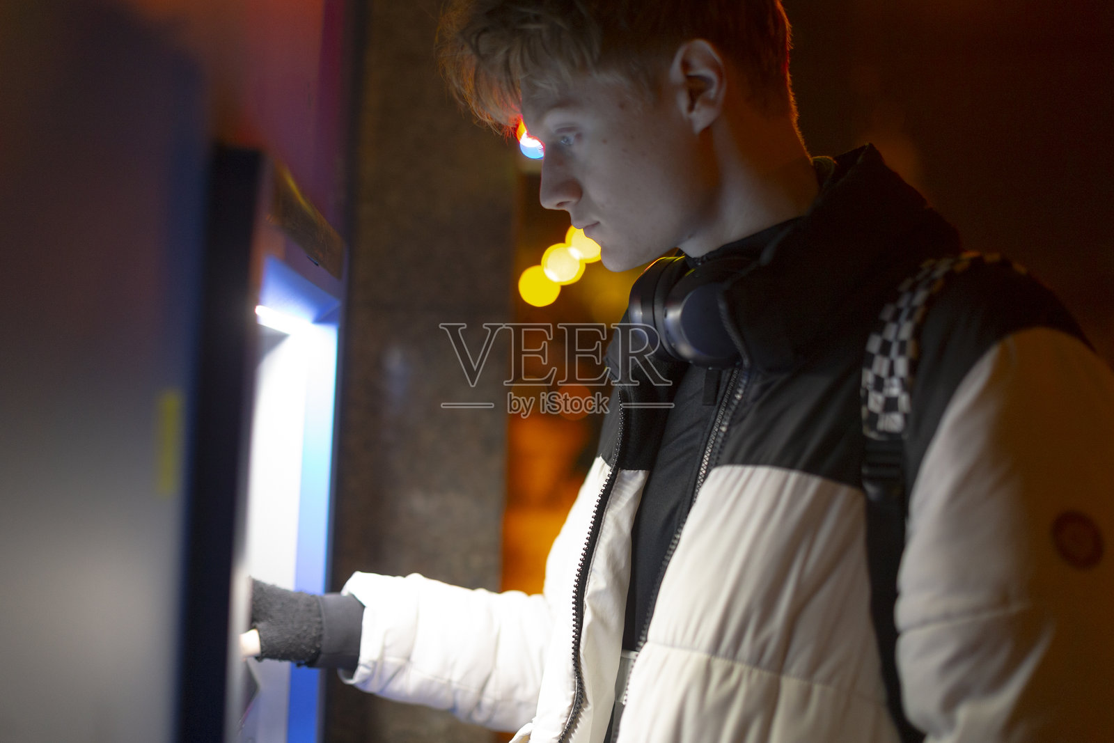 夜晚，霓虹灯下，年轻人在城市环境中操作自动售票机照片摄影图片