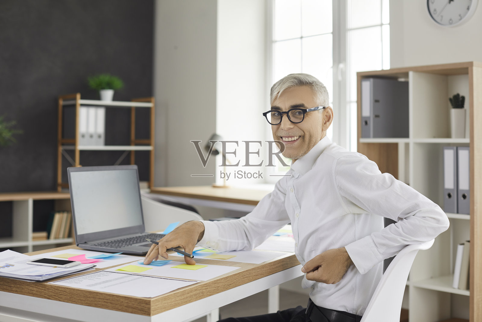 一位年长的商人正在办公室开发业务项目，并在彩色便签上写下笔记。照片摄影图片