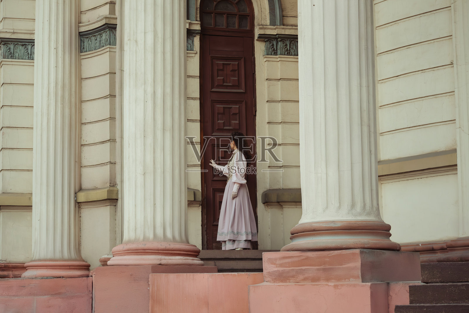 一位优雅的女士身着复古连衣裙，站在古老的石柱旁照片摄影图片