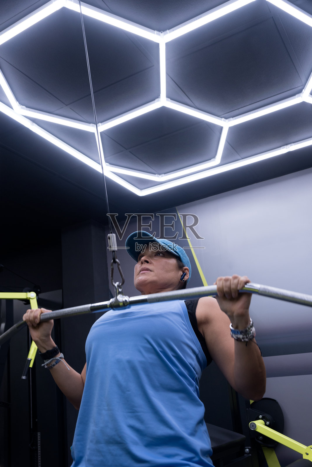 一位40岁的女性正在使用配有杠铃的滑轮训练器进行手臂和胸部训练。照片摄影图片