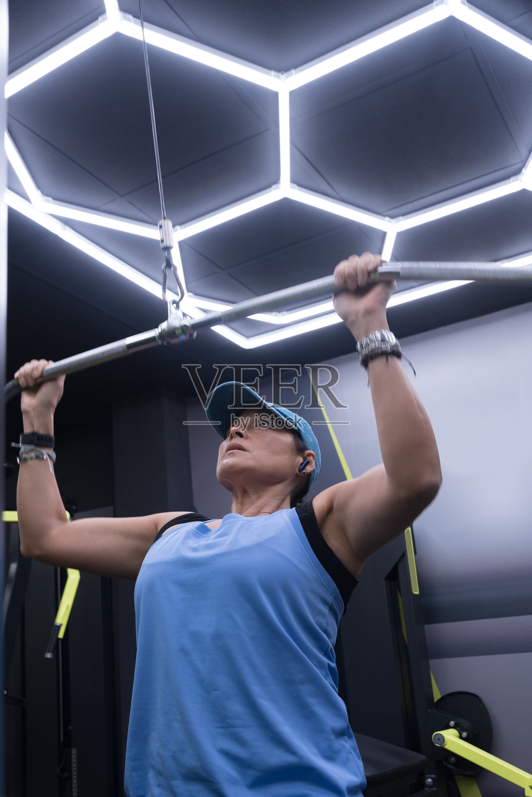 一位40岁的女性正在使用配有杠铃的滑轮训练器进行手臂和胸部的力量训练。照片摄影图片