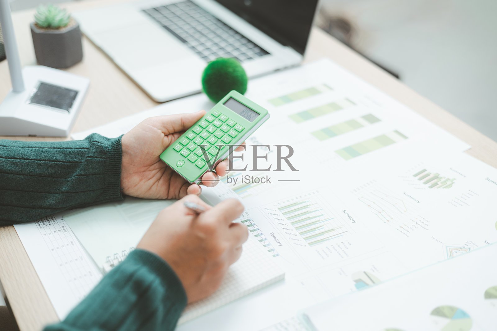 特写：一只手在金融图表上使用绿色计算器，旁边有一个地球仪，象征着可持续金融、绿色商业规划、环境会计和清洁经济增长。照片摄影图片