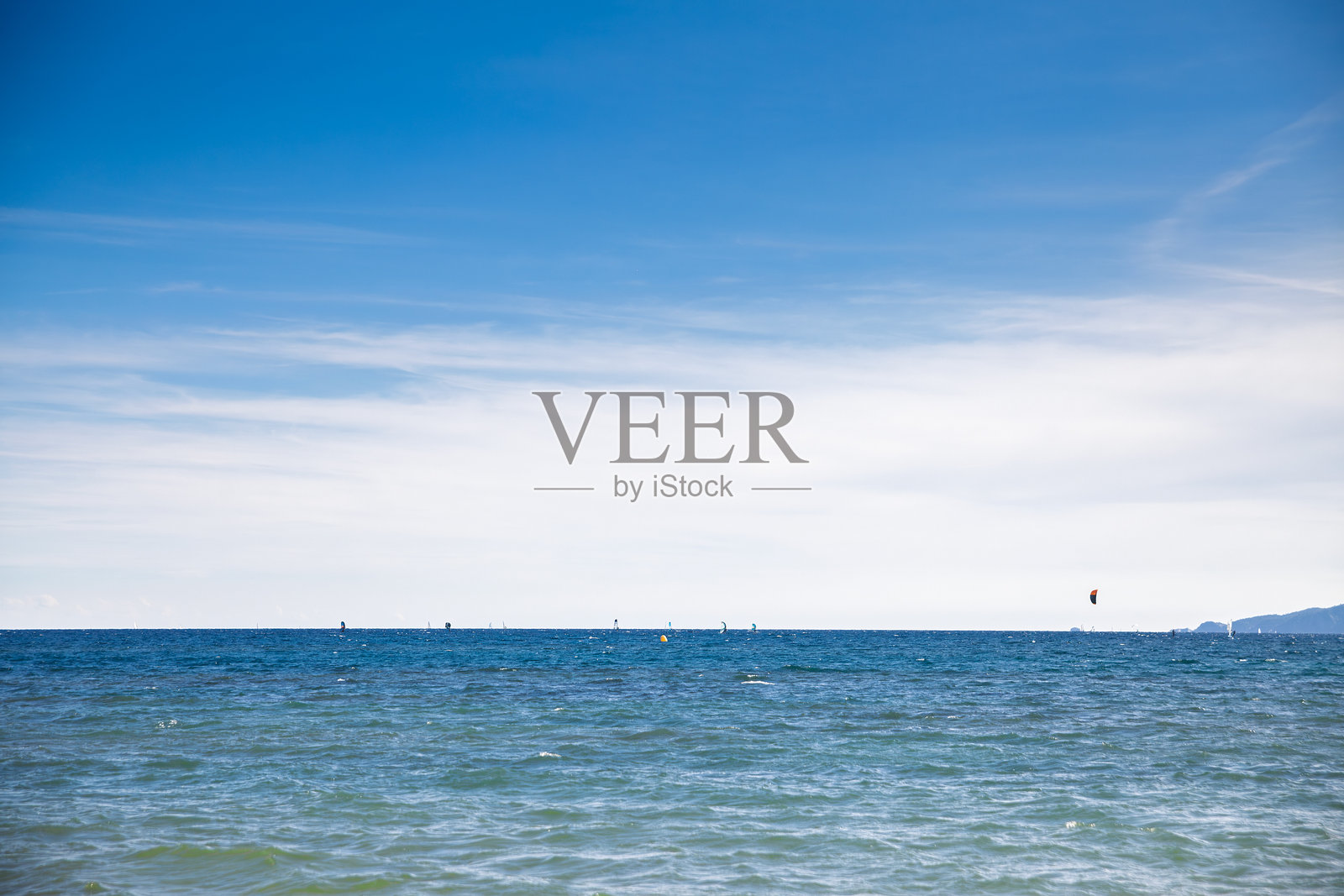 法国蔚蓝海岸的极简海景，展现地中海的远方，有小型帆船和远处的风筝冲浪者，天空广阔蔚蓝。平静的海浪和开阔的水域营造出宁静的氛围。照片摄影图片