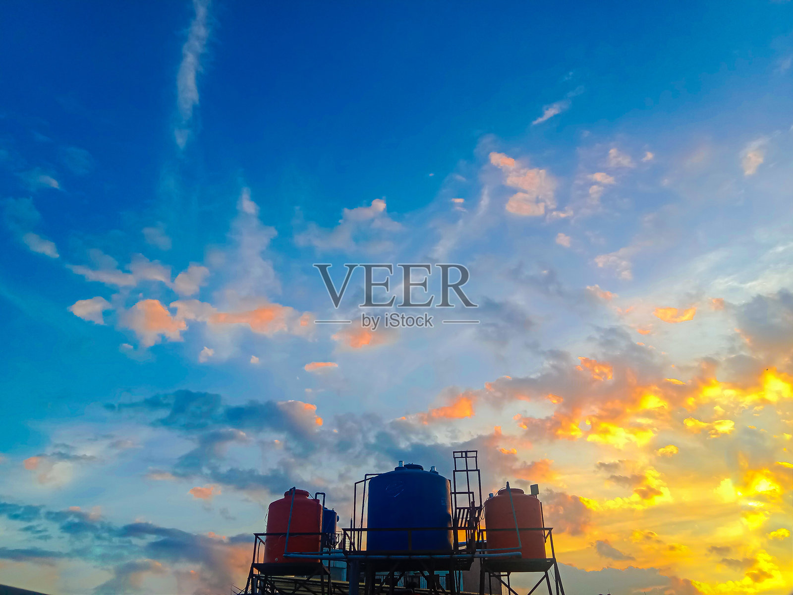 夕阳的天空呈现蓝色、橙色和黄色调，并有水箱的剪影照片摄影图片