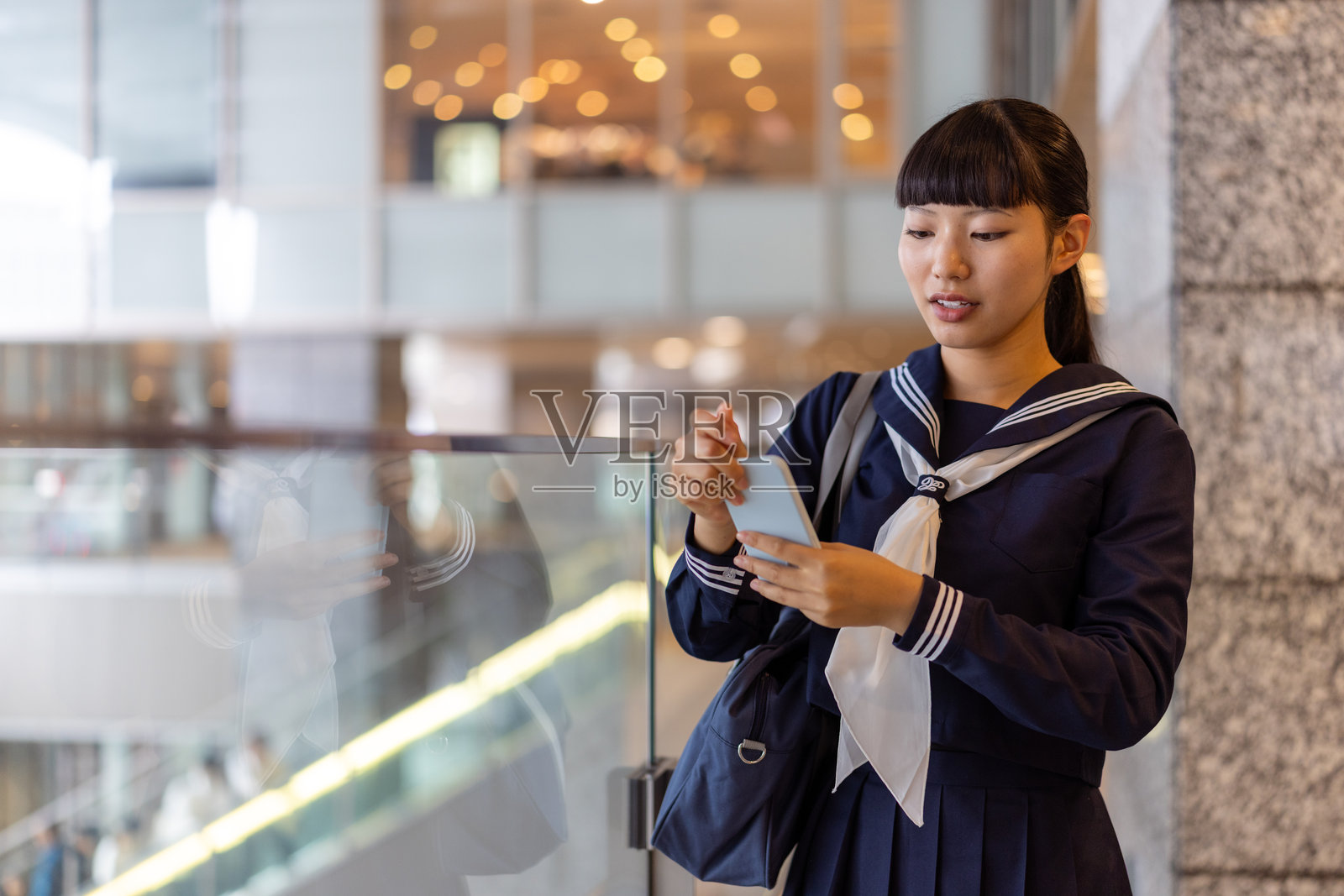 放学后，一名高中女生靠在城市的玻璃栏杆上照片摄影图片