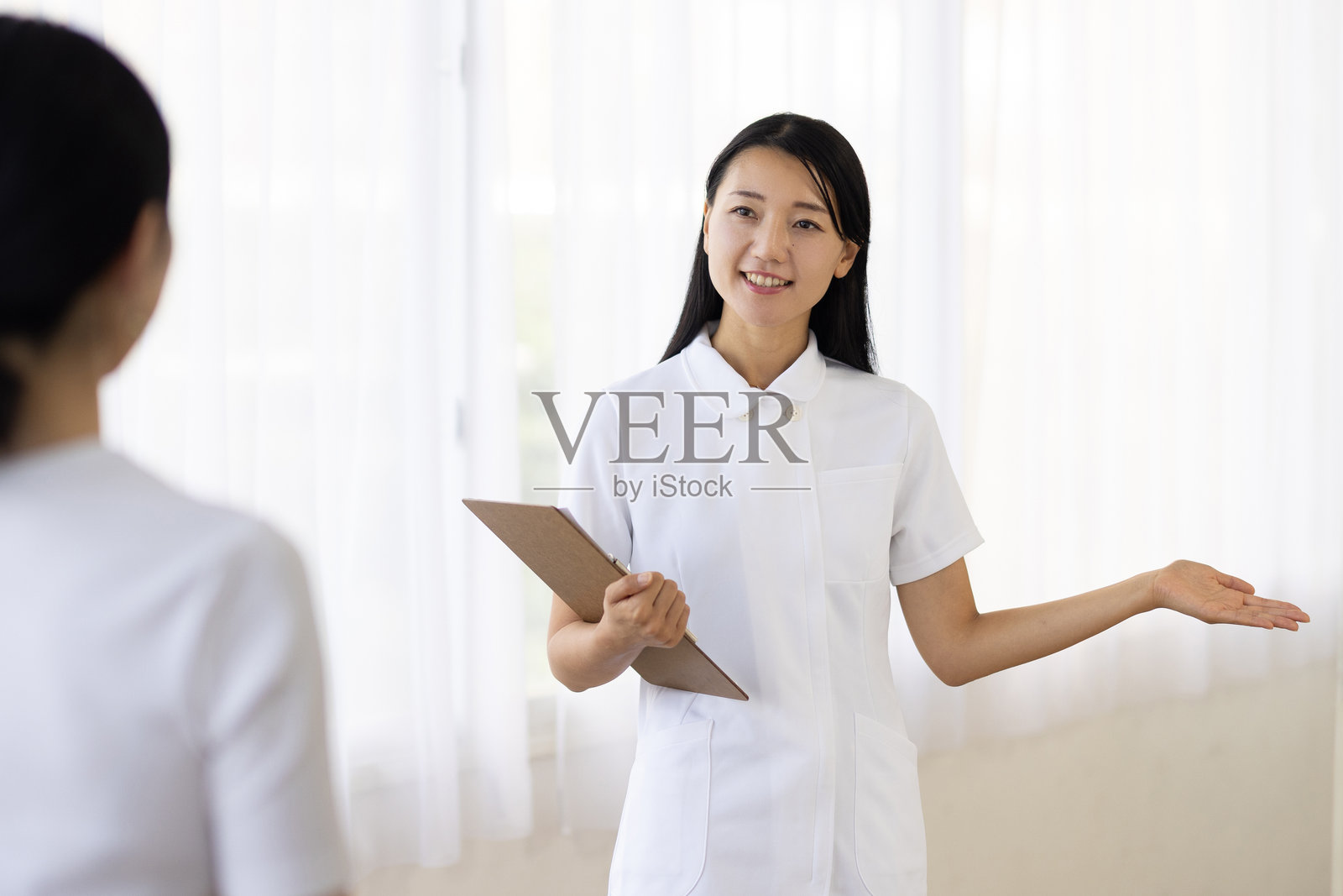 身穿白色制服的女性医务人员，手持文件板指导患者照片摄影图片