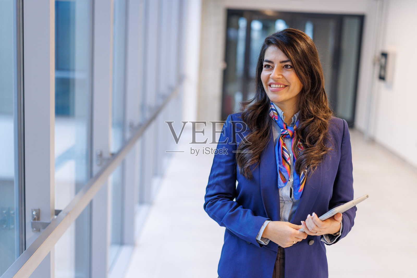 一位女士在公司走廊里边走边笑，手里拿着平板电脑工作。照片摄影图片