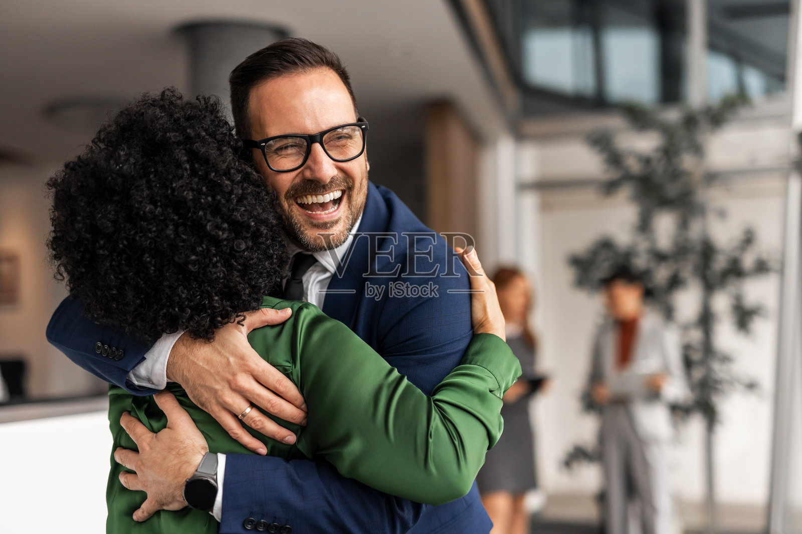 两位商务专业人士在明亮的办公室环境中开心地拥抱照片摄影图片