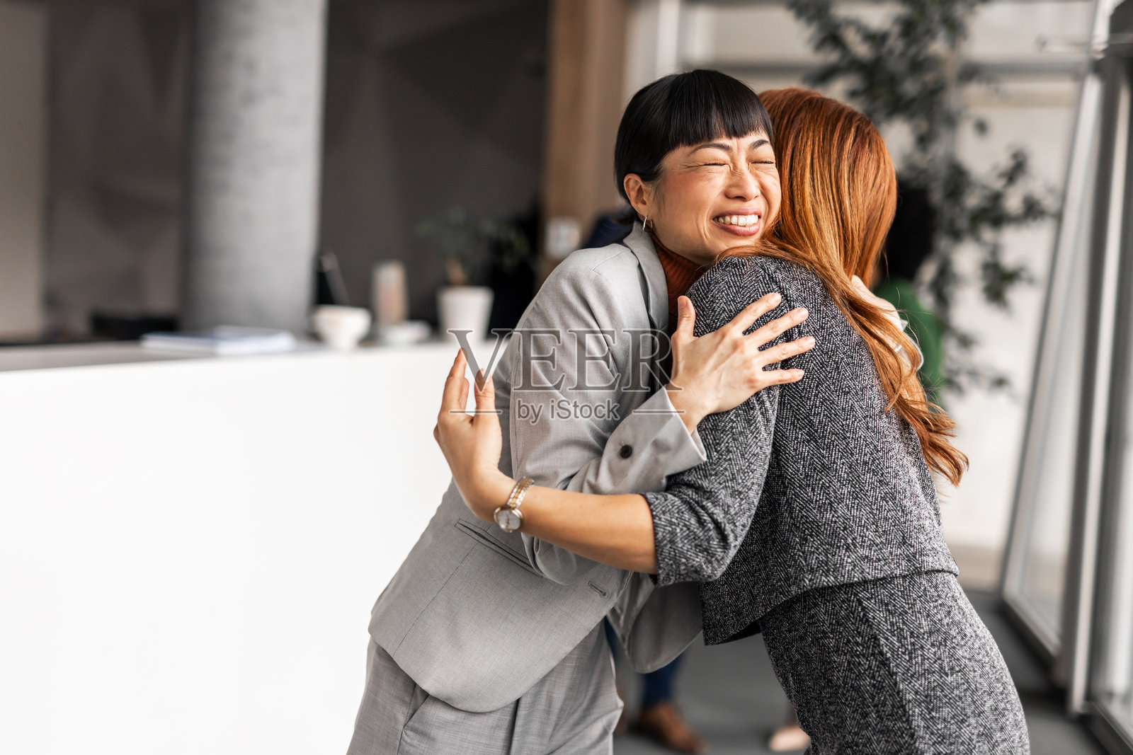 两位女商人亲切拥抱，背景是现代办公空间照片摄影图片
