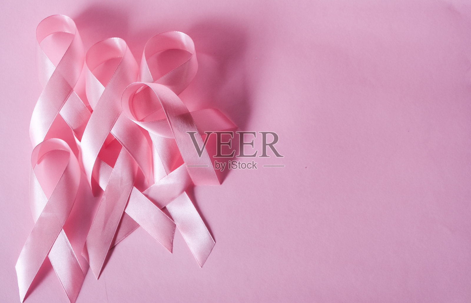 粉色丝带特写，粉色背景下孤立的粉色丝带，象征着乳腺癌的防治意识。照片摄影图片