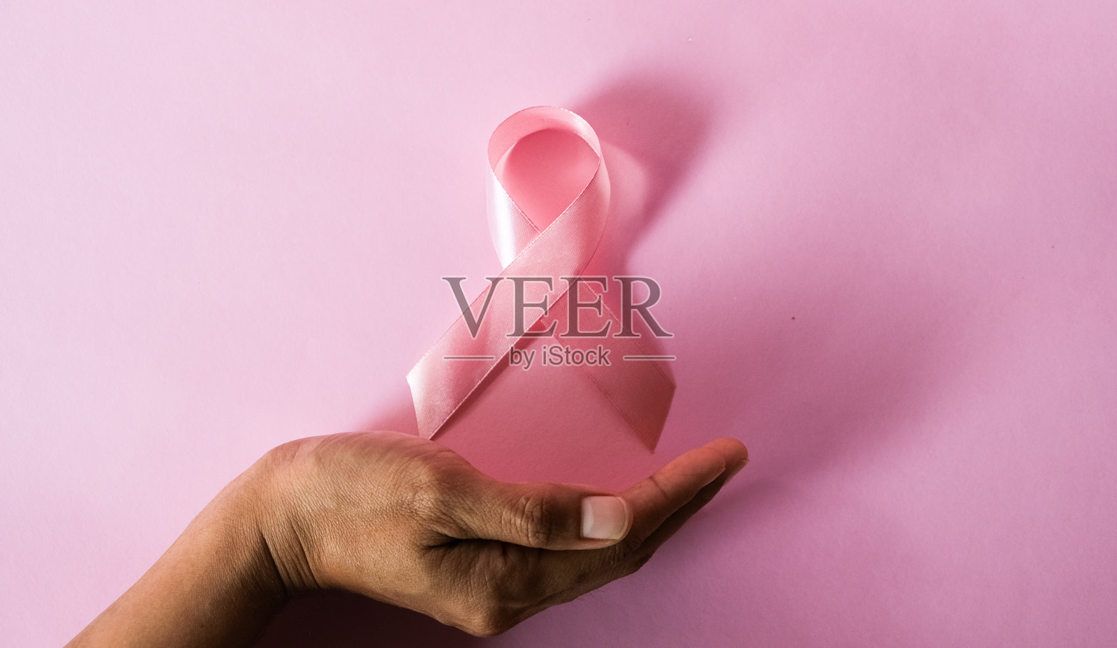 特写一位女性的手，手中拿着象征乳腺癌防治意识的粉色丝带照片摄影图片