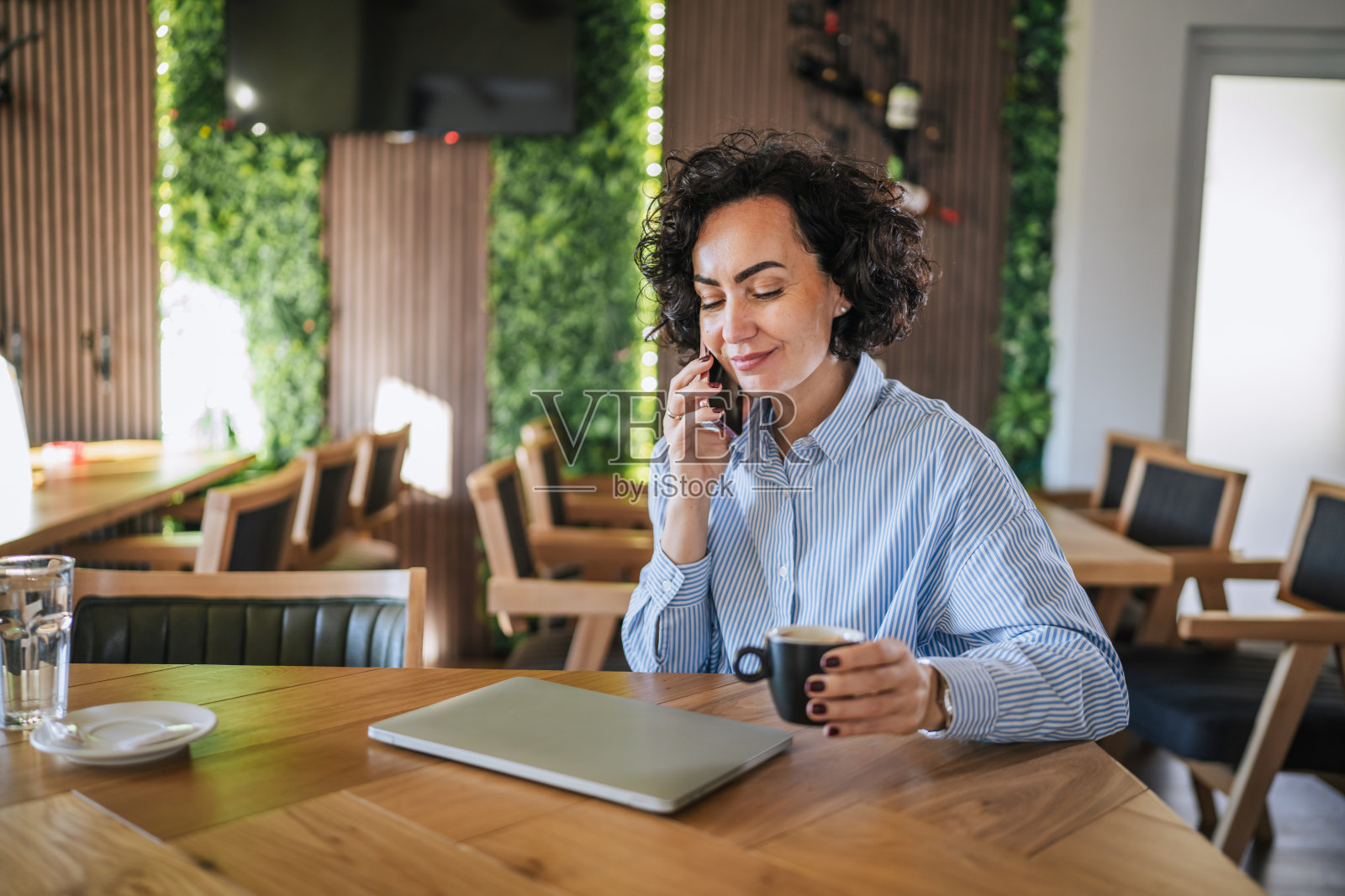 Businesswoman talking on phone and working remotely in cafe照片摄影图片