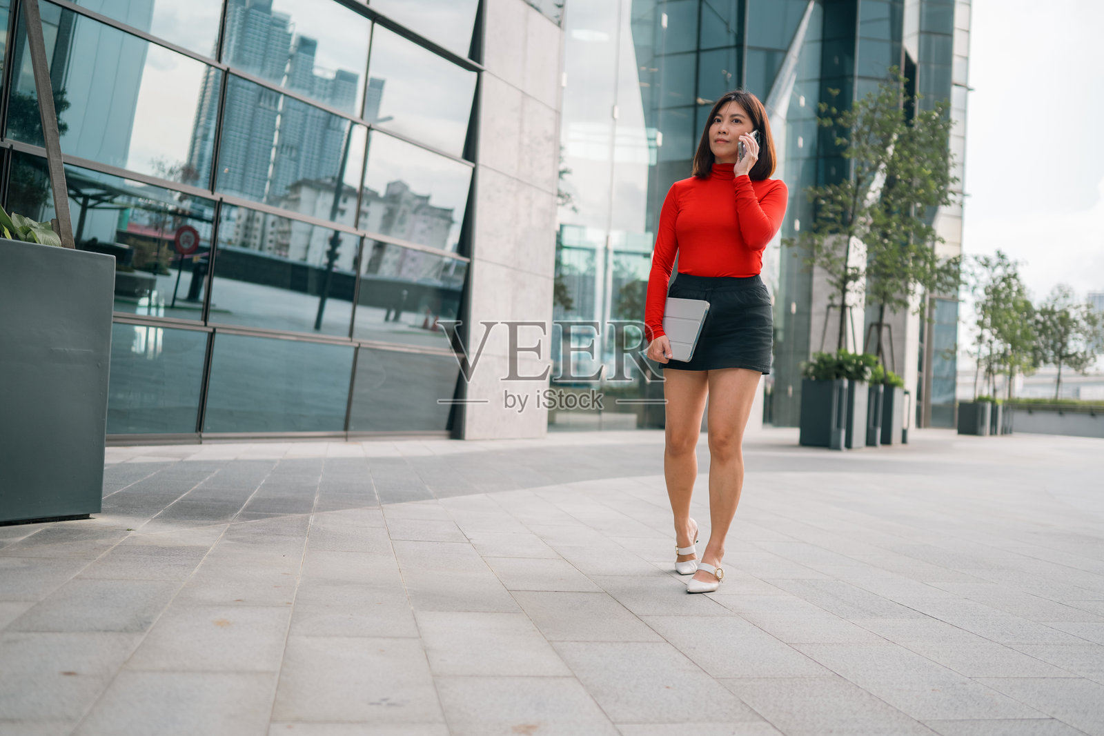 一位穿着红色套装的亚洲女商人在街头的抬高走道上打电话——现代都市生活方式概念。照片摄影图片
