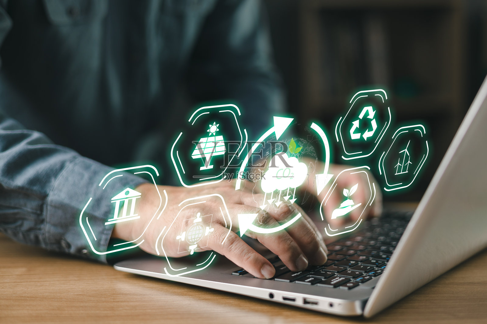 一个人正在用笔记本电脑打字，周围漂浮着象征可持续性、可再生能源、碳减排、绿色技术以及数字化创新中的环境责任的生态图标。气候变化照片摄影图片