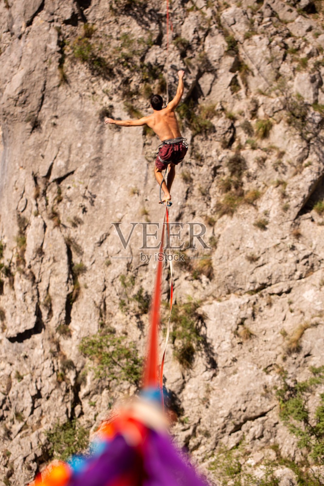 白天，一个人在明媚的日光下，在两座悬崖之间的一根绳索上走钢丝，背景是群山。照片摄影图片