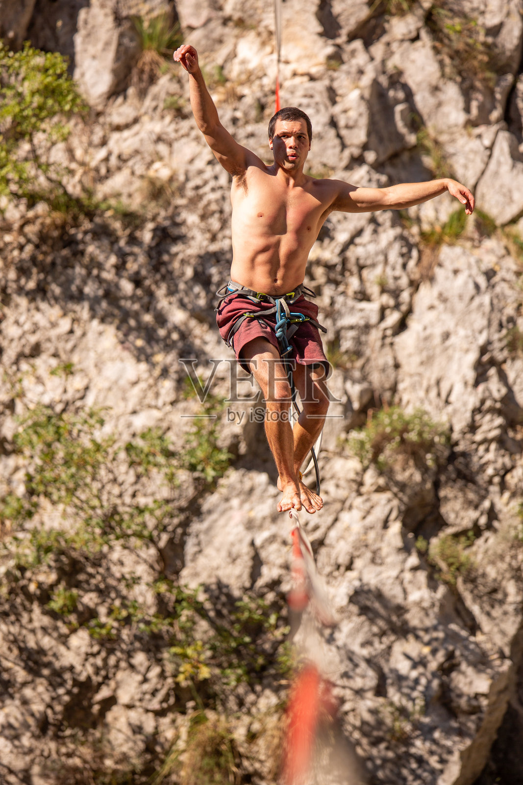 白天，一个人在自然户外环境中，走在高低不平的岩石地形上方的绳索上照片摄影图片