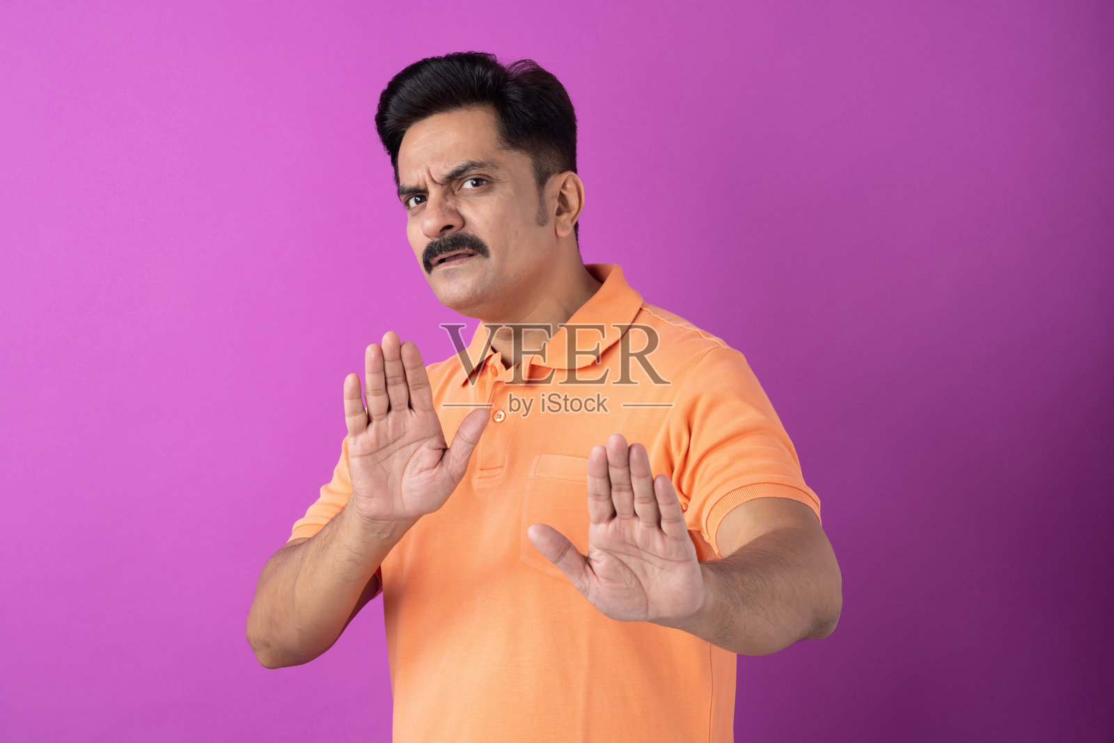身穿橙色T恤的印度中年男子，在紫色背景上隔离的样张照片摄影图片