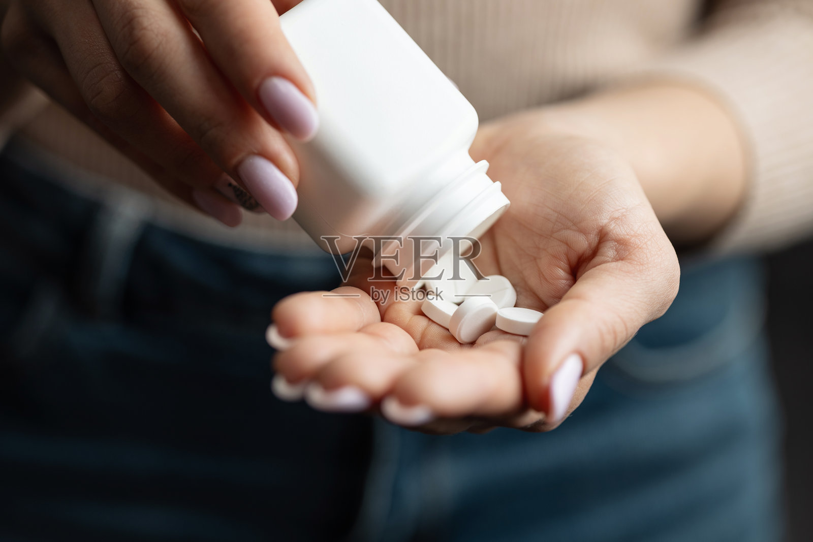 特写女性双手从药瓶中倒出白色圆形药丸，象征药物和药物治疗照片摄影图片
