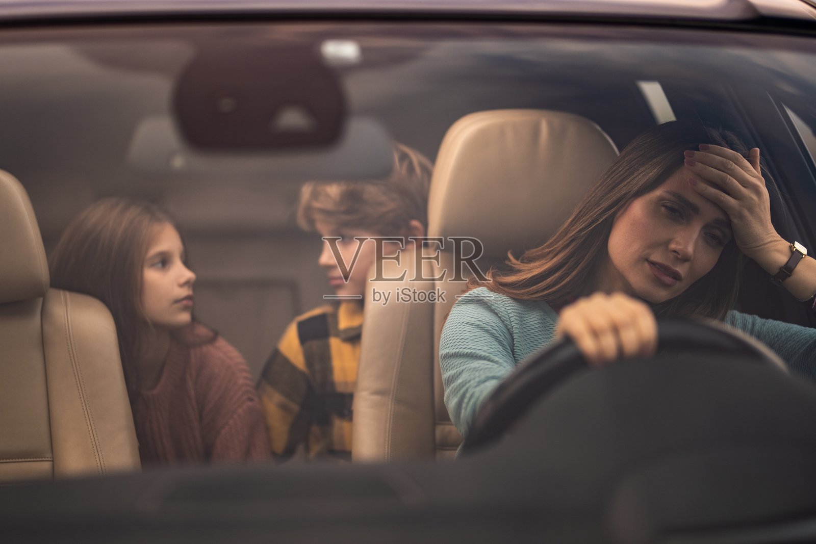 焦虑的母亲开车，孩子们坐在后座照片摄影图片