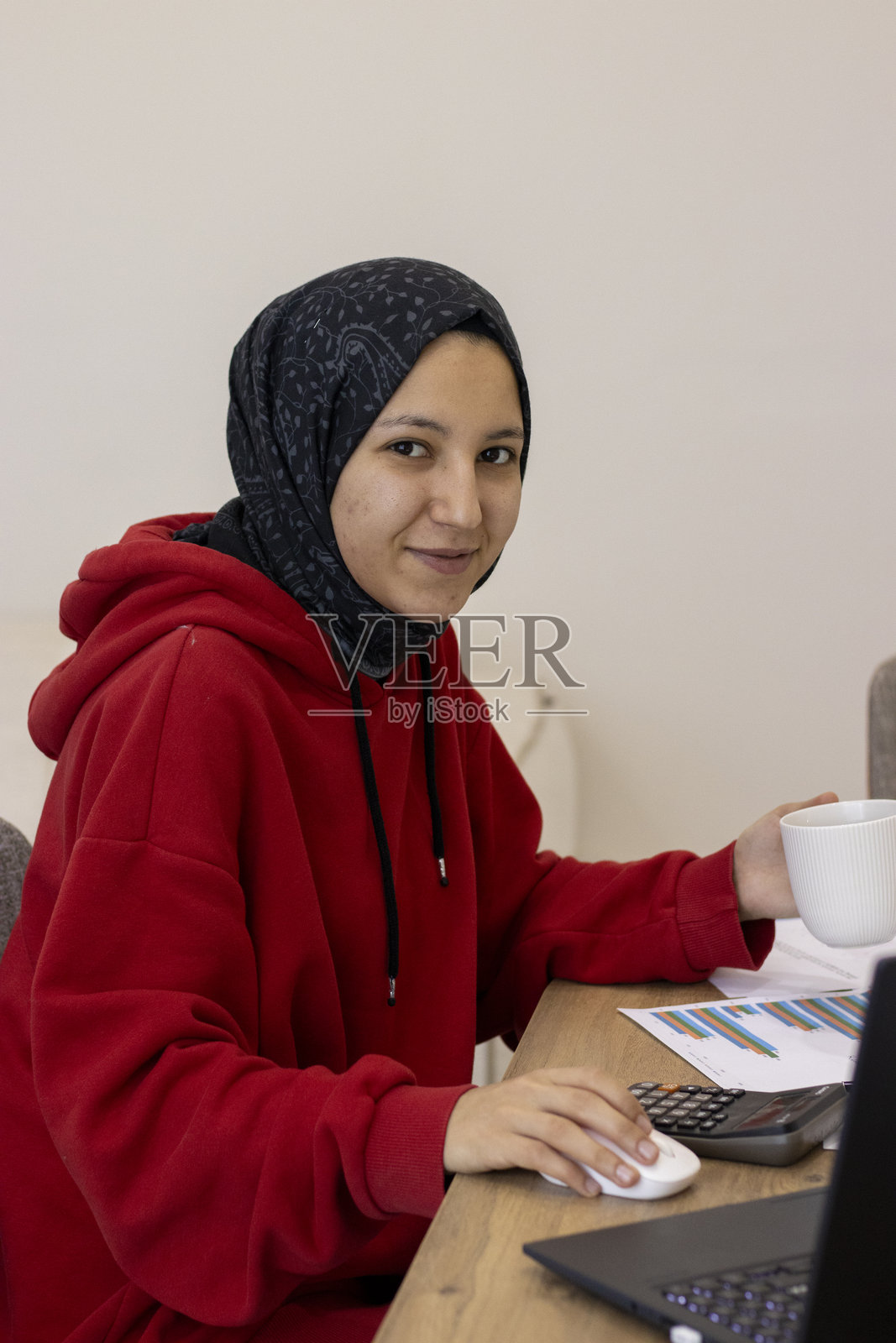 年轻女子戴着头巾，侧身在家里的书桌旁写文件，旁边放着咖啡杯和文具，居家办公空间，专注的活动，远程工作和规划，旨在提高生产力和生活方式设计照片摄影图片