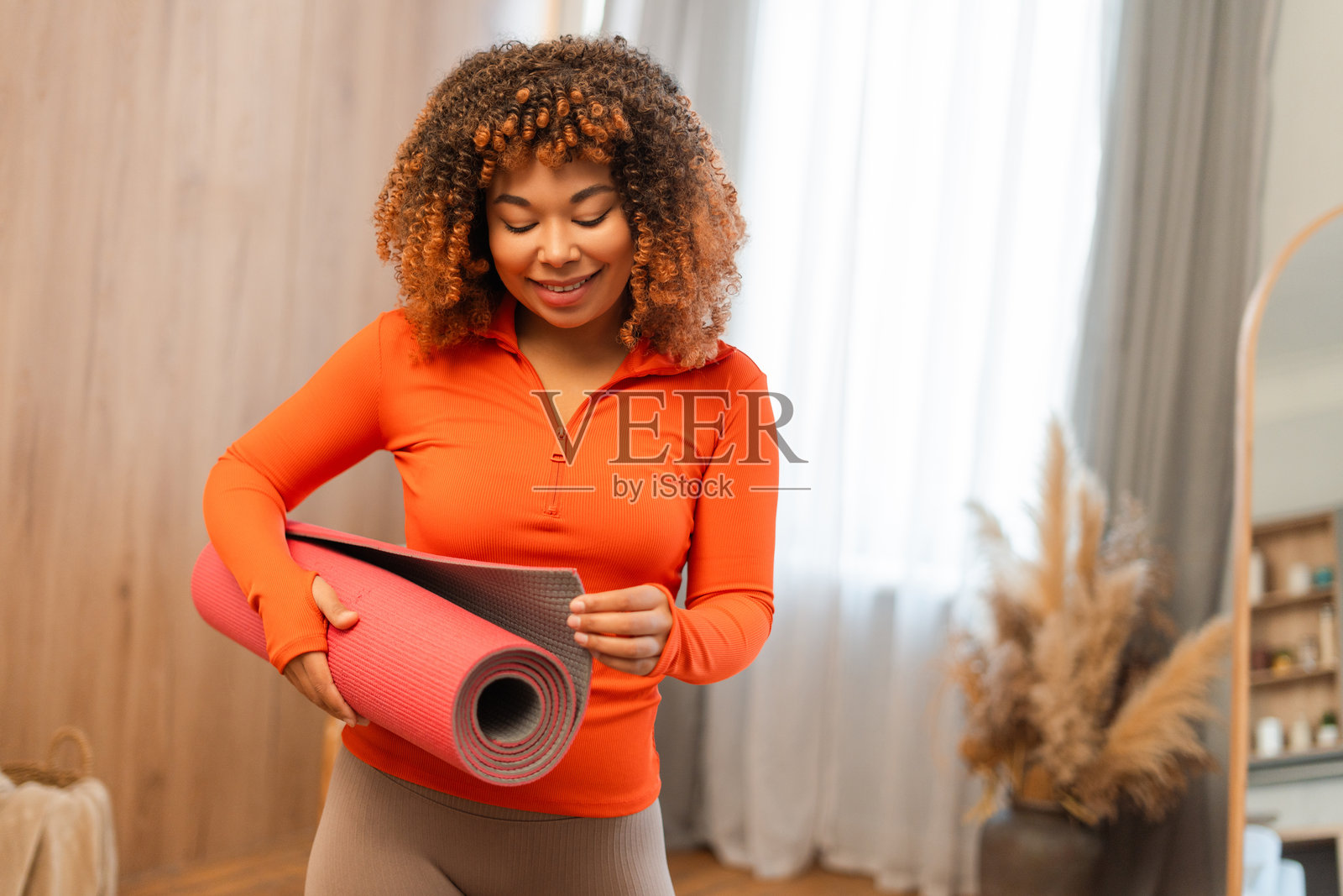 年轻女子在家卷起瑜伽垫，准备进行健康锻炼照片摄影图片