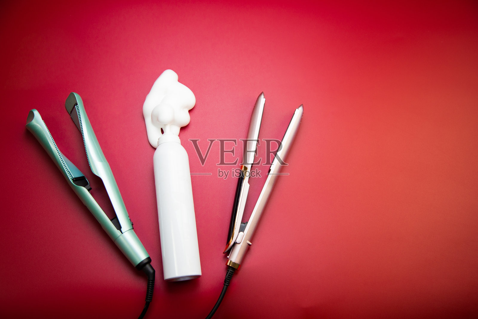 背景为粉色，留有文字空间，旁边放着一瓶白色造型摩丝，周围散落着直发器和卷发棒，用于打造卷发造型。该概念涉及头发护理、发型设计和发量增加，以及美发沙龙。照片摄影图片