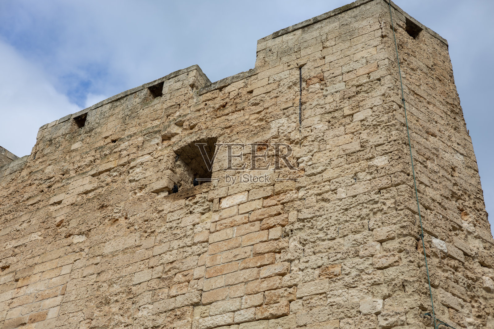 古老的石灰岩堡垒墙，具有饱经风霜的砌体、箭孔和中世纪防御塔，天空多云。非常适合历史旅行主题。照片摄影图片