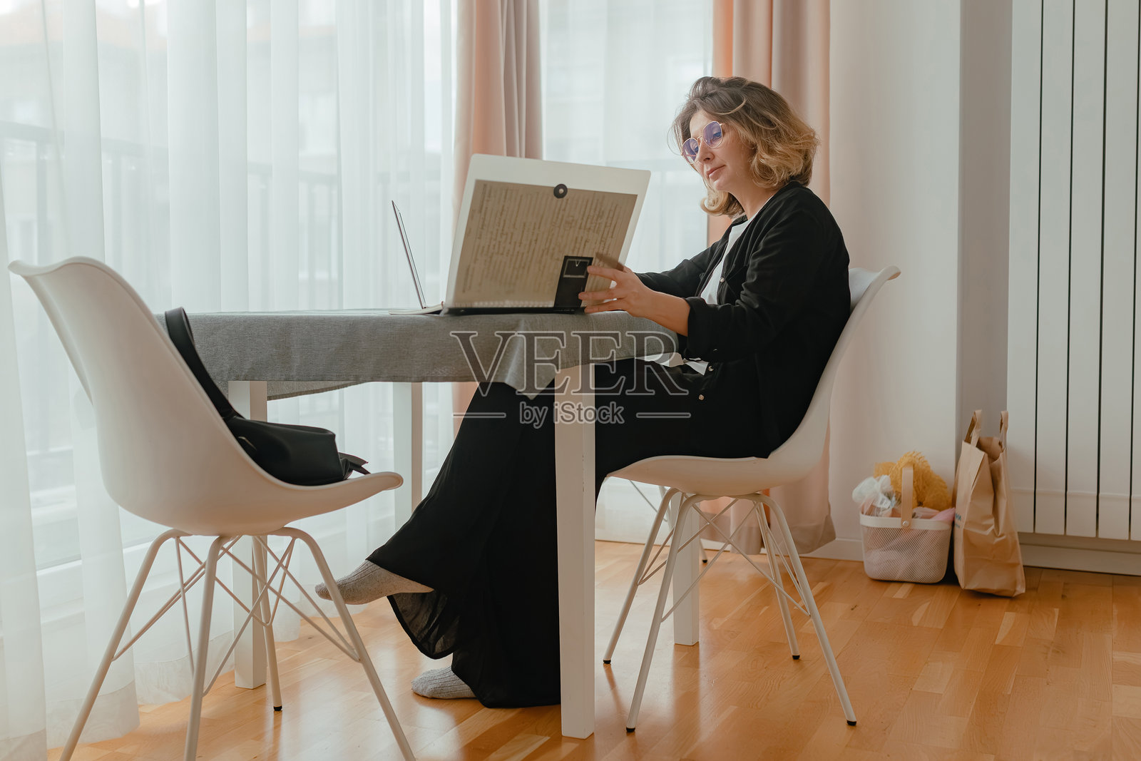 女人在笔记本电脑旁阅读厚厚的活页夹，明亮的窗帘，干净的工作空间里洒满日光，在家工作时姿势放松。照片摄影图片