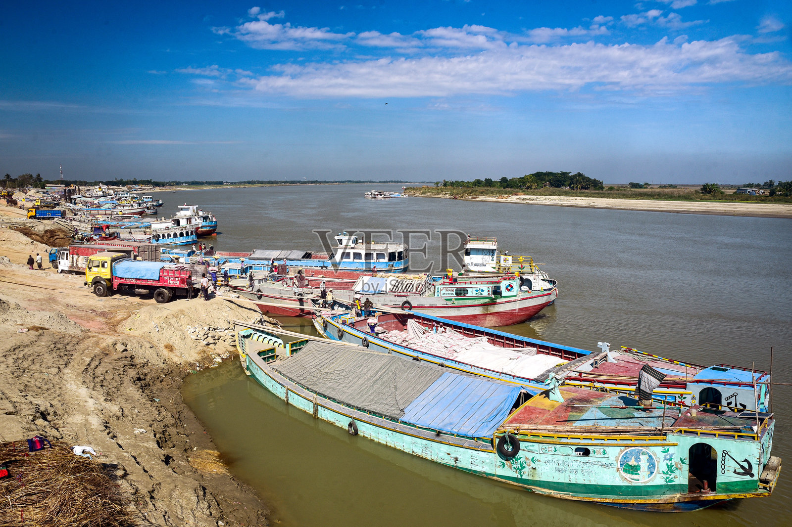 蓝天下平静的水道,色彩缤纷的船只停靠在泥泞的岸边照片摄影图片