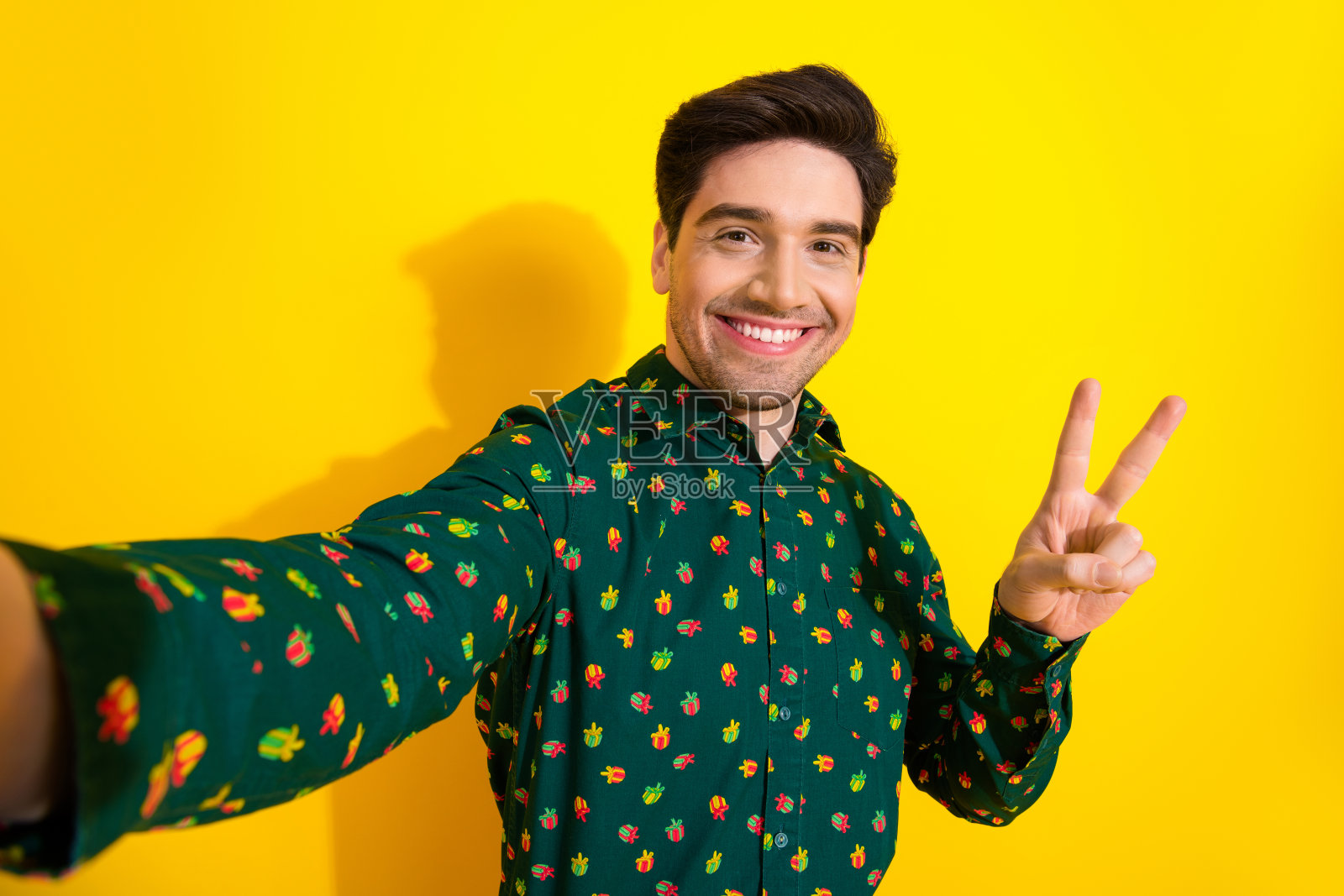 身穿绿色仙人掌图案衬衫的年轻男子，在明亮的黄色背景前快乐地自拍，用于时尚生活和广告宣传照片摄影图片