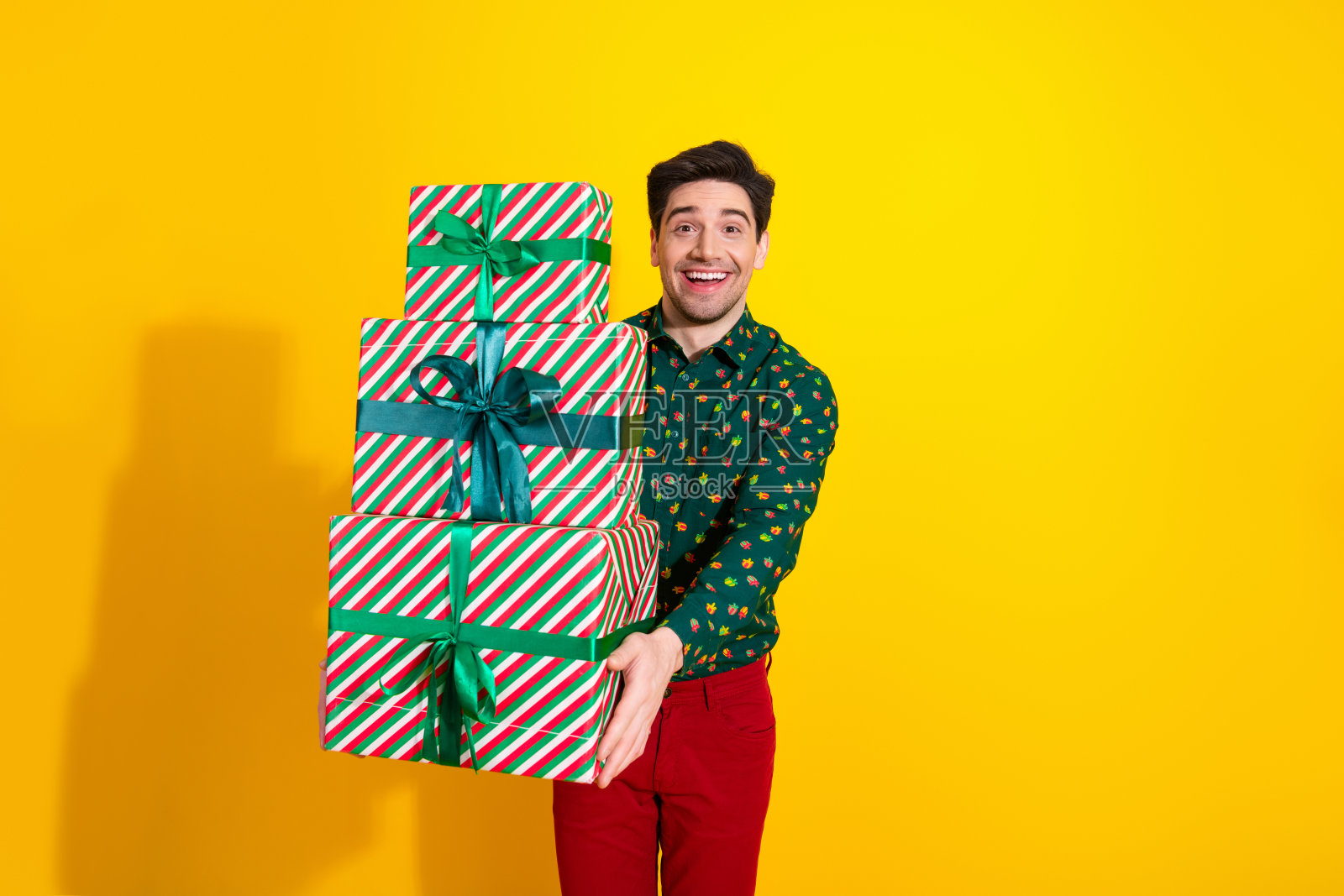 在明亮的黄色影棚里，一位年轻男子抱着一叠色彩鲜艳的条纹礼品盒，适合节日庆典和促销活动照片摄影图片
