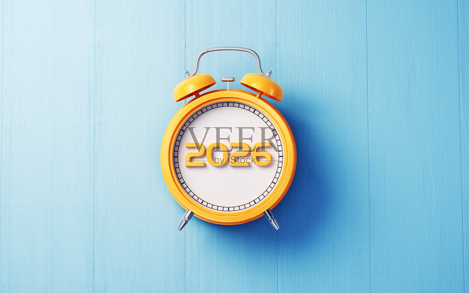 一个黄色的闹钟，放在浅蓝色的木质背景上，白色表盘，顶部写着黄色的2026年份。照片摄影图片