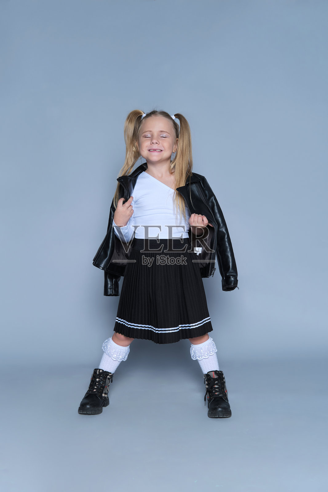 一位自信的年轻女孩肖像照，她身着现代服饰，包括皮夹克、黑色靴子和百褶裙。她大胆的姿态和俏皮的表情，使其成为儿童时尚、生活方式或肖像摄影的完美素材。照片摄影图片