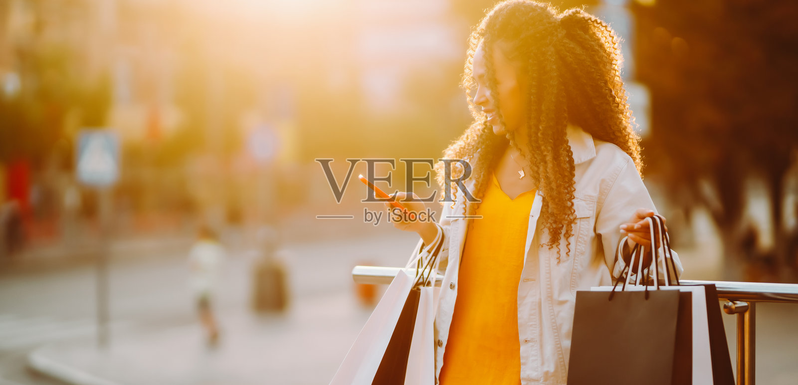 一位笑容满面的女士身着时尚服装，提着购物袋，在商店背景下享受阳光明媚的一天。照片摄影图片