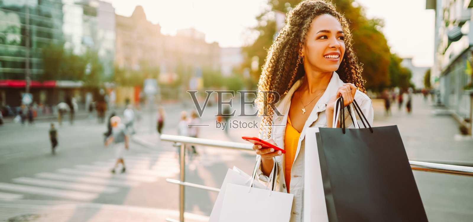 一位笑容满面的女士穿着时尚的衣服，提着购物袋，在有商店作为背景的阳光明媚的日子里享受着。一位笑容满面的女士穿着时尚的衣服，提着购物袋，在有商店作为背景的阳光明媚的日子里享受着。照片摄影图片