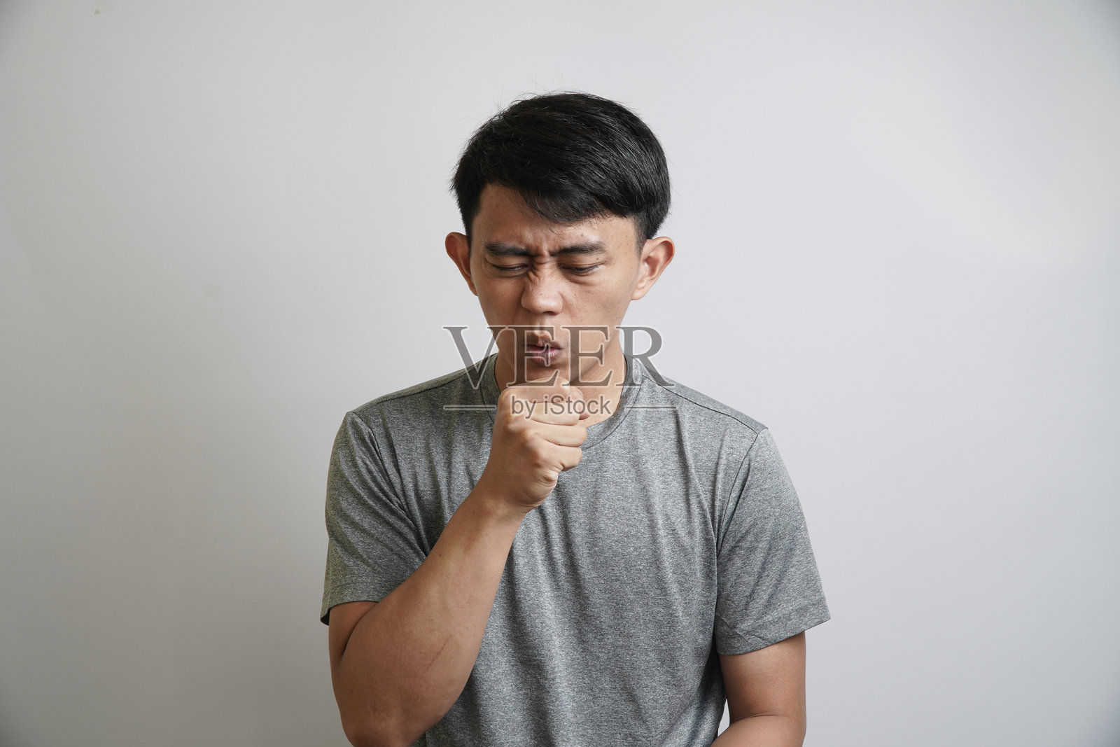 生病的年轻亚洲男子闭着眼睛，用拳头捂嘴咳嗽照片摄影图片