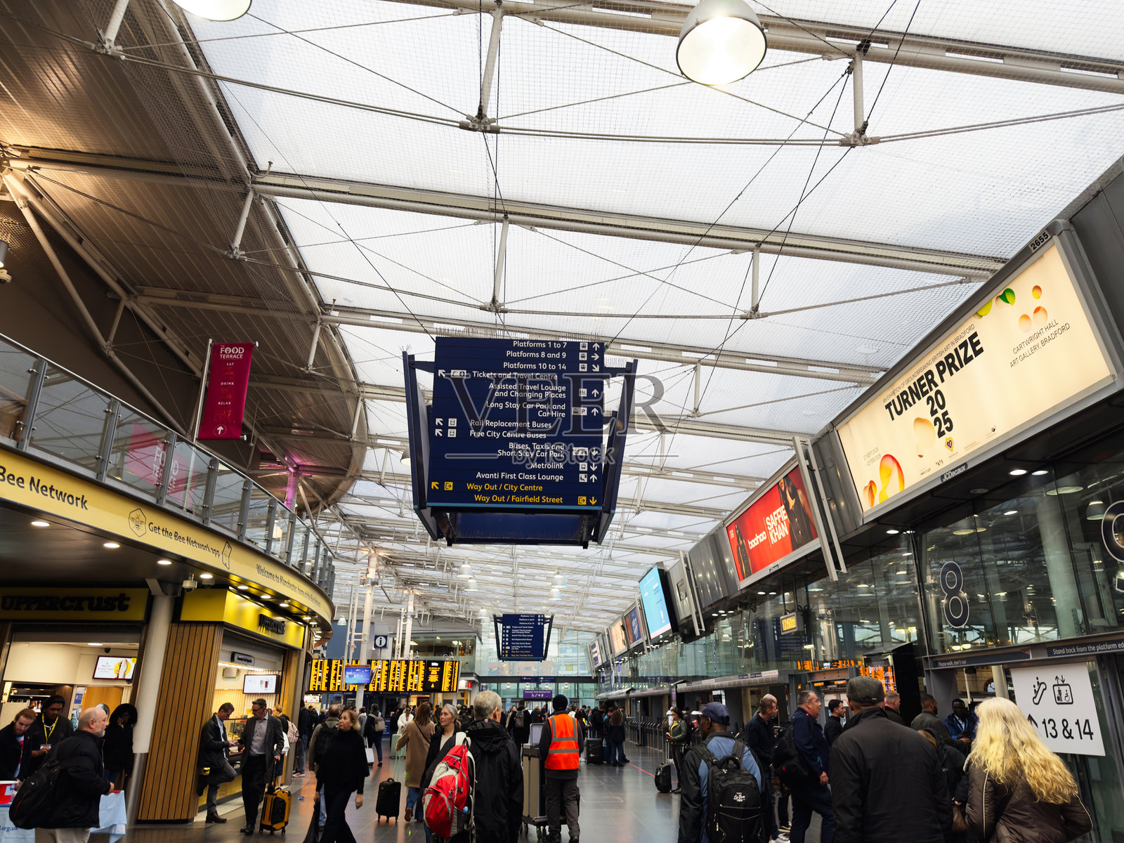 繁忙的曼彻斯特机场候机大厅,有指示牌、旅客、行李和商店,上方是玻璃天花板照片摄影图片